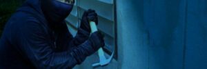 A robber in a black outfit attempts to break into a home at night using a hammer